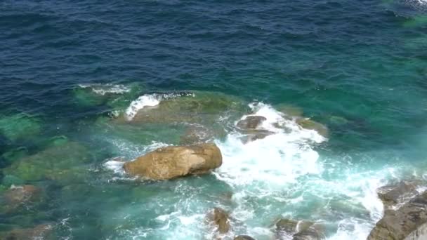 Ondas espumosas quebram em uma costa rochosa em um dia ensolarado e claro — Vídeo de Stock