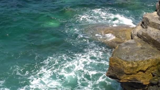 Foamy waves break on a rocky shore on a sunny, clear day — Stock Video