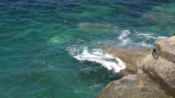 Пенные волны ломаются на скалистом берегу в солнечный ясный день — стоковое видео