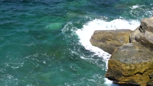 Foamy waves break on a rocky shore on a sunny, clear day — Stock Video