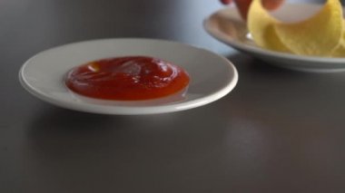 Bir adam baharatlı domates sosu ile patates cips yiyor, sulu her. Gri bir masada. Yemek beyaz tabaklarda