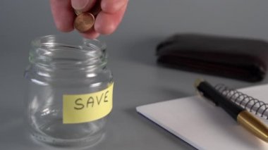 Bir el tasarruf cam bir kavanoza para sent ve euro atıyor yazıt Kaydet ile. Sırada defter, kalem, deri cüzdan var. yavaş çekim