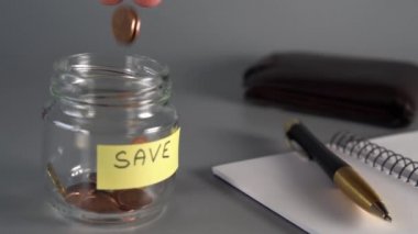 El tasarruf cam bir kavanoza para sent atma yazıt Kaydet. Sırada defter, kalem, deri cüzdan var. Finansal emeklilik tasarruf kavramı. yavaş çekim