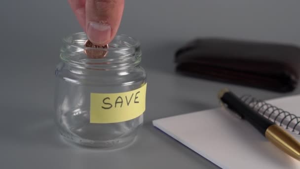 一只手把硬币和欧元扔进一个装有 字样的储蓄罐中 笔记本 皮革钱包是下一个 为未来储蓄节省经济的概念 — 图库视频影像