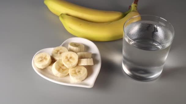 スライスし バナナ全体 白い皿の上に灰色の背景に表示されます きれいな水で霧に包まれた 健康的なライフスタイルの概念 — ストック動画