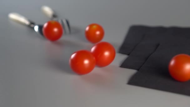 红熟的樱桃西红柿在灰色背景上滚动 仍然用勺子 叉子和三个黑色餐巾纸生活 蔬菜饮食概念 — 图库视频影像