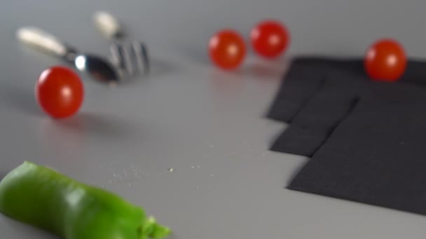 緑のピーマンのスライスは灰色の背景に落ち スプーン フォーク チェリートマトと3つの黒ナプキンと静物 野菜料理を調理するというコンセプト — ストック動画