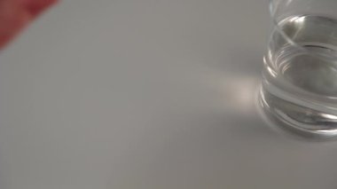 Bir el, bir bardak suyun yanındaki gri bir masaya bir avuç beyaz tıbbi kapsül döker. İlaç ve besin takviyeleri almaya hazırlık