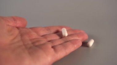 Beyaz tıbbi kapsüller bir elin avuç üzerine düşmek, sıçrayan ve gri bir masaya aşağı yuvarlanan. Antibiyotik kullanımı kavramı. Yavaş çekim