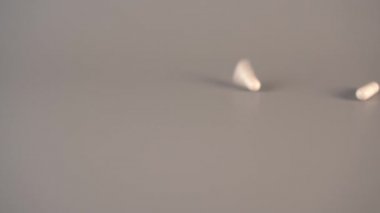 Beyaz tıbbi kapsüller gri bir tablo üzerinde yukarıdan düşmek. Homeopatik ilaçların kullanımı kavramı. Yavaş çekim