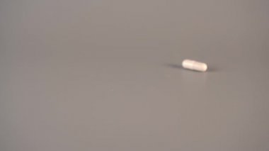 Koyu ve beyaz tıbbi kapsüller gri bir tablo üzerinde yukarıdan düşmek. Doğal ilaçların kullanımı kavramı. Yavaş çekim