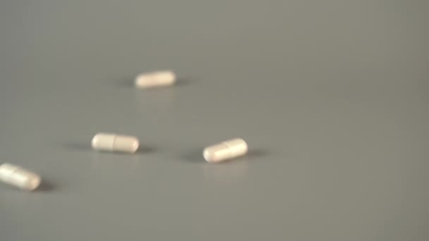 Capsules médicales blanches glissent vers le bas du revêtement gris. Concept de supplémentation en glutamate sodique. Mouvement lent 