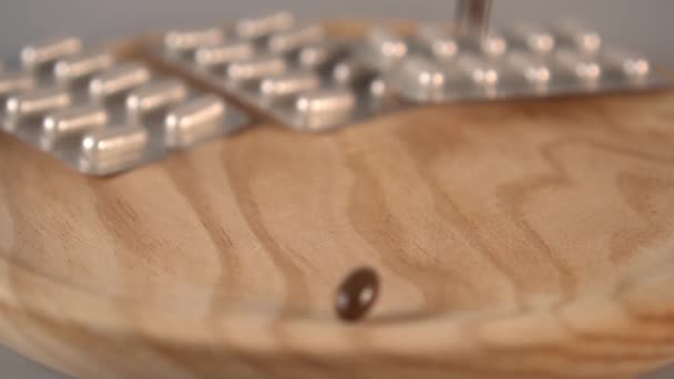 Capsules médicales sombres et blanches tombent sur une surface en bois sur un fond gris. Packs de médicaments en arrière-plan. Mouvement lent 