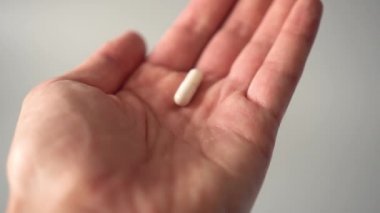 Tıbbi beyaz kapsüller avucunuzun içine düşer ve bazıları uçar. gri arka planda
