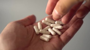 Bir el seçer ve tıbbi beyaz kapsül bir avuç alır ve oral uygulama için yükseltir. gri arka planda