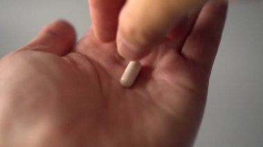 Bir el bir avuç tıbbi beyaz kapsül alır ve oral uygulama için yükseltir. gri arka planda