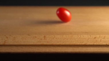 Kiraz domates ahşap bir yüzeye düşer. Siyah bir arka plan üzerinde. Yavaş çekim. Pişirme Sebze Diyet Yemekler