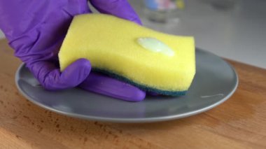 Temizlik maddesinin bir kısmı sarı-yeşil bir süngerin üzerine damlar. El sıkıyor ve kalın köpük gri bir plaka üzerine akar. Ahşap bir yüzeyde. Yavaş çekim