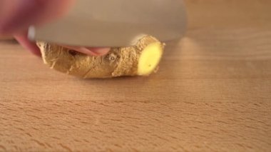 Bir adam sulu bir zencefil kökünü bıçakla parçalara ayırır. Tahta bir tahtanın üzerinde. Doğal Soğuk Çare Pişirme