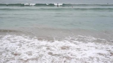 Akşam okyanus sörfü. Köpüklü dalgalar kumlu plajı doldurur. Sörfçüler dalgayı salladı. Büyük bir grup bekliyor