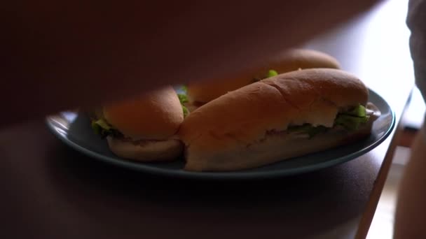 新鮮なサンドイッチは 灰色のテーブルの上にアクアマリンプレートに横たわっています 女の子は家から取り外すための箔にパックします 自家製ファーストフード — ストック動画