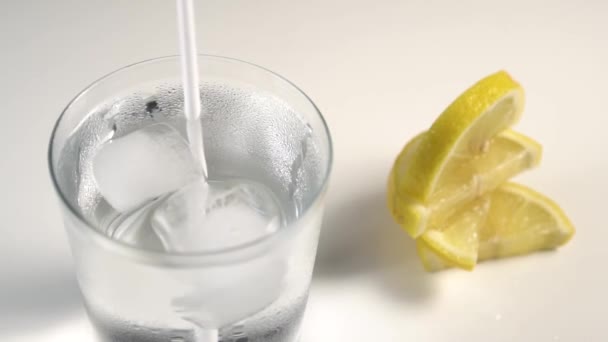 白い背景に蒸しガラスで回転する氷の立方体とチューブ 次にジューシーなレモンのスライスを置く — ストック動画