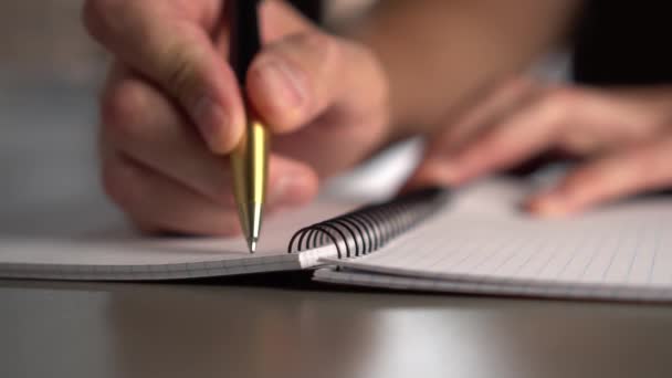 一个男人在灰色的桌子上用黄色黑色笔在打开的笔记本上写字 窗户上的灯照亮了工作场所 慢动作 — 图库视频影像