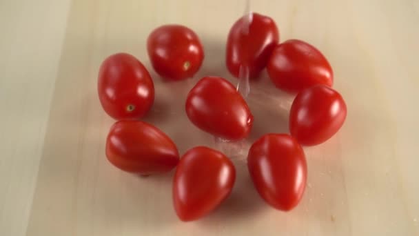 几个红色的多汁樱桃西红柿在木质表面旋转 洗涤的水流从上面滴落 烹饪素食菜肴 — 图库视频影像