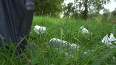 genç adam gri bir çanta içinde çim üzerinde plastik çöp toplar. Plastik çöp ile gezegenin doğasının kirlilik sorunu