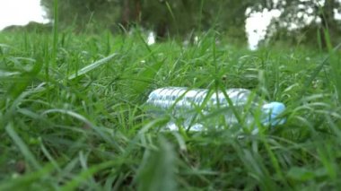 Plastik çöp yeşil genç çim üzerine çim üzerine düşüyor. Doğada çöpe atılan çöp sorunu