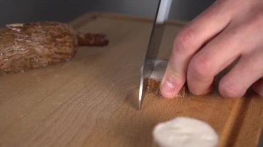 Genç bir adam gri bir masaüzerinde ahşap bir mutfak tahtası üzerinde bir bıçak ile bir yucca kökü keser. Evde sağlıklı yemekler pişirmek