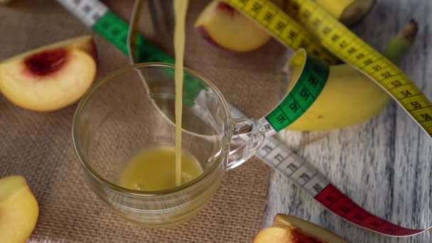 Персиковый сок наливают в стакан. На столе персики и сантиметр на мешковине — стоковое видео