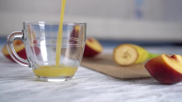 Persika saft hälls i en glas mugg på ett träbord med skivade persikor — Stockvideo