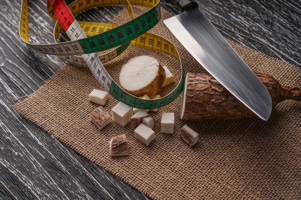 Radice di yucca affettata su un sacco su un tavolo di legno con un coltello e un centimetro — Foto Stock