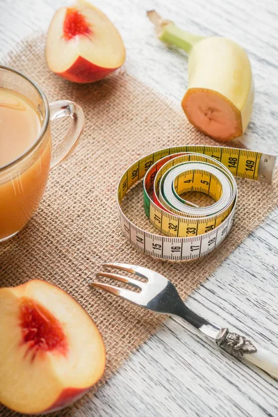 白い木製のテーブルの上に、果物とフォークとセンチメートルの袋の上に桃ジュースのグラス — ストック写真