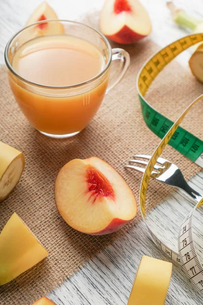 Un bicchiere di succo di pesca su un sacco su un tavolo di legno bianco con fette di frutta e una forchetta e un centimetro — Foto Stock