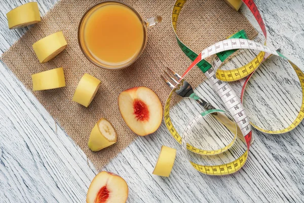 白い木製のテーブルの上に、果物とフォークとセンチメートルの袋の上に桃ジュースのグラス — ストック写真