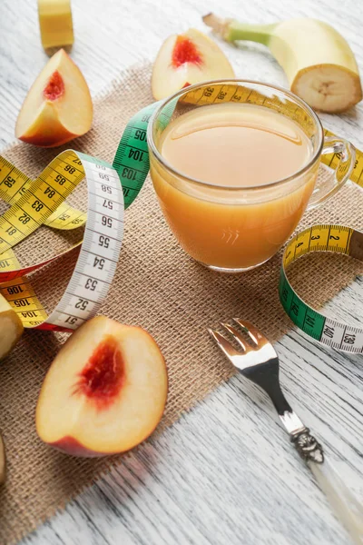 Un bicchiere di succo di pesca su un sacco su un tavolo di legno bianco con fette di frutta e una forchetta e un centimetro — Foto Stock