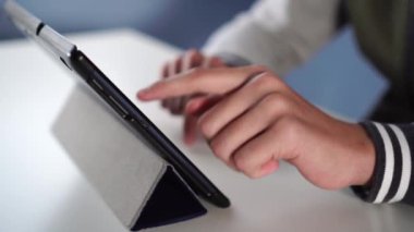 Spor kazaklı bir genç mavi duvara karşı beyaz bir masadaki deri mavi bir stantta tablet kullanıyor. Sosyal ağlar ve bilgisayar oyunları kullanmanın faydaları ve zararları kavramı