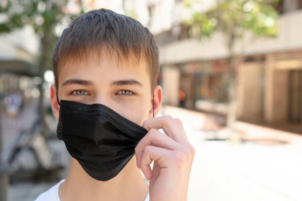 Sad young man takes off a medical black mask near the road on an empty city street without people. Alone. Copyspace. Close-up. Coronavirus protection concept