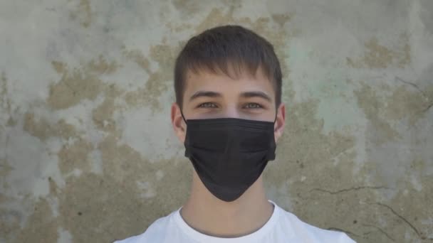 Jovem Tira Uma Máscara Protetora Médica Preta Contra Uma Parede — Vídeo de Stock