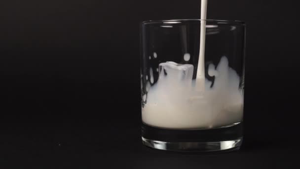 Frische Milch in ein Glas mit Eiswürfeln auf schwarzem Hintergrund gießen. Zeitlupe spritzt mit Tropfen frischen weißen nahrhaften Getränks aus nächster Nähe. Zeitlupe.