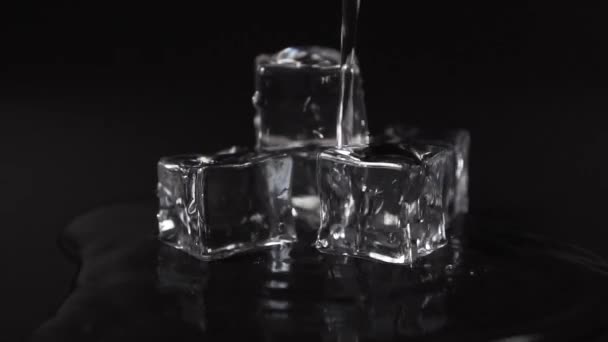 黒い表面の澄んだ水の流れの下で氷のキューブが溶けます スパークリング冷凍コンセプト — ストック動画