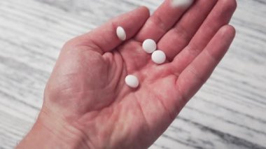 Beyaz ilaç hapları avucunun içine yavaş yavaş düşüyor. Hafif ahşap zemin. Tıbbi konsept