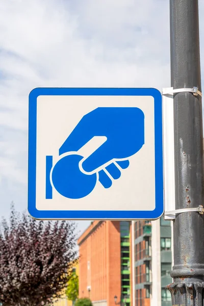 Paid parking payment road sign. On a gray iron rusty post on a city street. Against the background of blue sky and buildings with trees