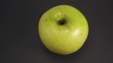Arka planda koyu yeşil bir elma var. Taş dokusu yüzeyi. Yavaş dönüş. Besleyici malzemeler.