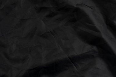 Yüzünde kırışıklıklar ve kıvrık kıvrımlar olan siyah bir madde. Buruşmuş sentetik kumaş. Soyut dramatik arka plan. Tasarım ve başlıklar için.