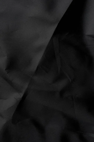 Abstract black synthetic material with wrinkles and wrinkled folds. Old wrapping dusty cloth. Crumpled dramatic texture background. For design and headlines.