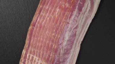 Karanlık bir taş yüzeyde ince domuz pastırması parçaları. Hızlı bir atıştırmalık için sulu tütsülenmiş et.