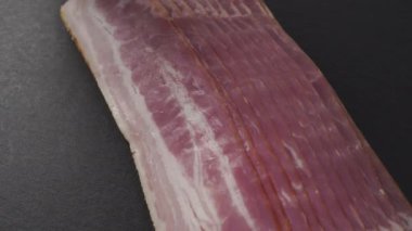 El, yağ tabakalı taze kırmızı pastırma şeridi alır. Siyah taş bir tahtanın üzerinde. Kesilmiş iştah açıcı et.